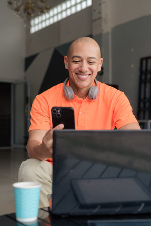 Hispanic man sitting and using laptop computer and phone in coffee shop restaurant