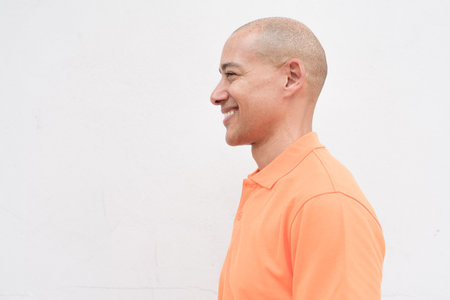 Studio portrait of handsome middle aged bald man face profie view in orange polo shirt against plain white wall background. Casual lifestyle and fashion concept.の写真素材