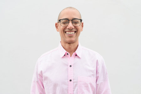 Bald Hispanic mature male in 40s wearing pink casual business shirt and eyeglasses standing in front...