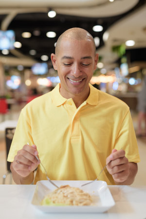 Portrait of a mature bald man sitting indoors at a modern food court restaurant eating healthy chicken rice.の写真素材