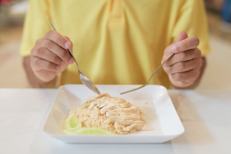 Close-up of man sitting at food court restaurant eating healthy Hainanese chicken rice wearing yellow polo shirtの写真素材