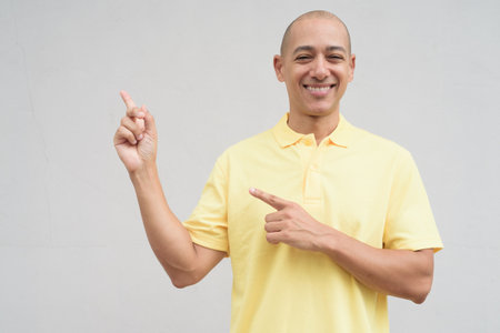Studio portrait of a handsome mature happy man with shaved head smiling wearing yellow polo shirt, standing in front of a neutral plain white wall with copy space.の写真素材
