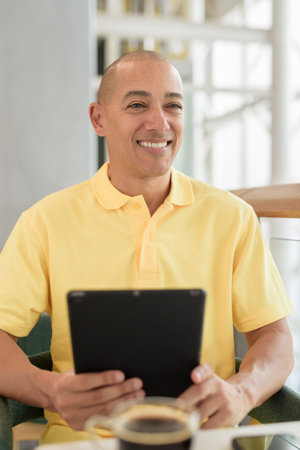Confident mature bald man sitting at a stylish cafe, while enjoying a coffee break during day using...