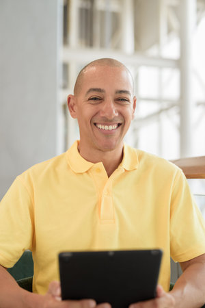 Confident mature bald man sitting at a stylish cafe,while enjoying a coffee break during day using digital tablet computer. Modern lifestyle and business concept.の写真素材