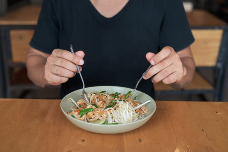 Portrait of a middle-aged bald tourist man enjoying traditional Thai pad Thai noodles at an outdoor...
