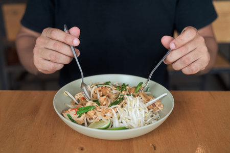Portrait of a middle-aged bald Hispanic tourist man enjoying traditional Thai pad Thai noodles at an...