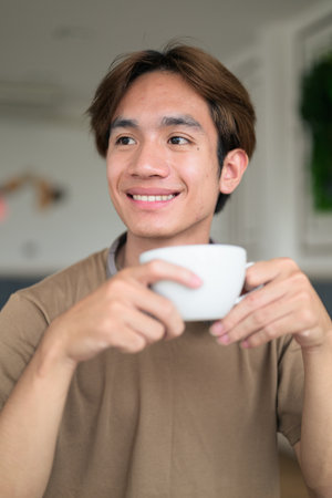 Young Thai student man in a brown t-shirt in coffee shop wearing headphones around his neck.の写真素材
