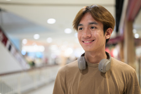 Young Thai man in a brown t-shirt with headphones around his neck.の写真素材