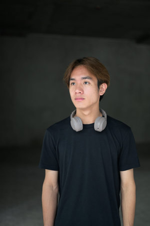 Young Thai Asian man wearing a black t-shirt, posing in a minimalist brutalist-style construction...