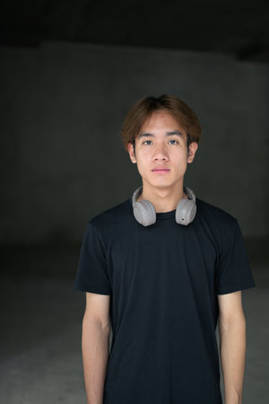 Young Thai Asian man wearing a black t-shirt, posing in a minimalist brutalist-style construction area with gray concrete walls concept of modern lifestyle, urban fashion and architectureの写真素材