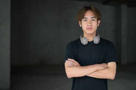 Young Thai Asian man wearing a black t-shirt, posing in a minimalist brutalist-style construction...