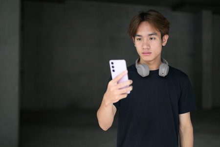 Young Thai Asian man wearing a black t-shirt, using phone in a minimalist brutalist-style...