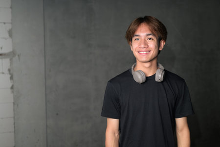 Young Thai Asian man wearing a black t-shirt, posing in a minimalist brutalist-style construction...