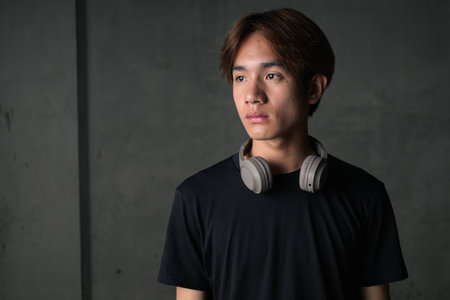 Young Thai Asian man wearing a black t-shirt, posing in a minimalist brutalist-style construction area with gray concrete walls concept of modern lifestyle, urban fashion and architectureの写真素材
