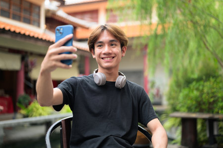 Young Thai Asian man sitting outdoors in traditional Chinese garden market. Confident, relaxed, and authentic look suitable for various concepts and usesの写真素材