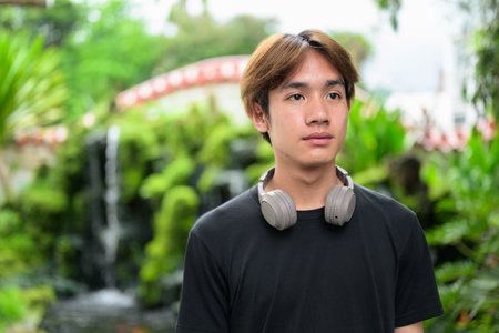 Young Thai Asian man in traditional Asian Zen garden during summer. Confident, relaxed, and authentic look suitable for various concepts and usesの写真素材