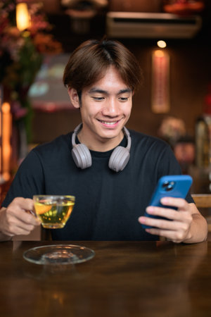 Portrait of a young Thai Asian man in casual style using phone in traditional Chinese style tea house restaurant. Confident, relaxed, and authentic look suitable for various concepts and usesの写真素材