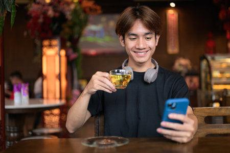 Portrait of a young Thai Asian man in casual style using phone in traditional Chinese style tea house restaurant. Confident, relaxed, and authentic look suitable for various concepts and usesの写真素材