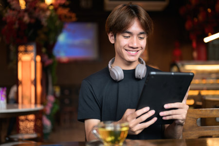 Portrait of a young Thai Asian man in Chinese style tea house using digital tablet computer and having hot tea. Portrait for modern lifestyle with onfident, relaxed, and authentic looksの写真素材