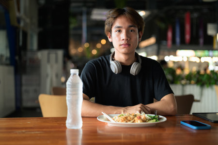 Pad Thai noodles eaten with chopsticks in Thailand by young tourist man during day. Famous street food cuisine loved by tourist and locals in Asia.の写真素材