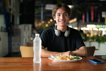 Pad Thai noodles eaten with chopsticks in Thailand by young tourist man during day. Famous street food cuisine loved by tourist and locals in Asia.の写真素材