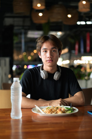 Pad Thai noodles eaten with chopsticks in Thailand by young tourist man during day. Famous street food cuisine loved by tourist and locals in Asia.の写真素材