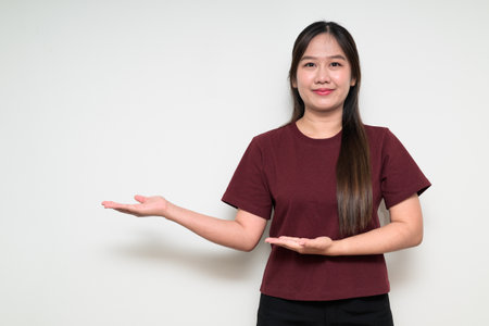 Studio portrait of young cute Asian woman presenting something against white background wearing casual t-shirtの写真素材