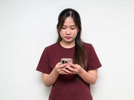 Studio portrait of young cute Asian woman using mobile phone against white background wearing casual t-shirtの写真素材