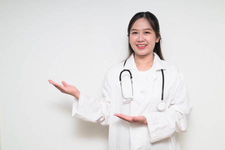 Studio portrait of Southeast Asian Thai healthcare worker woman doctor in lab coat against white background posing confidentlyの写真素材