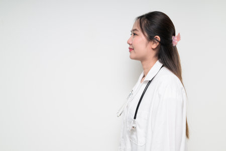 Studio portrait of Southeast Asian Thai healthcare worker woman doctor in lab coat against white background posing confidentlyの写真素材