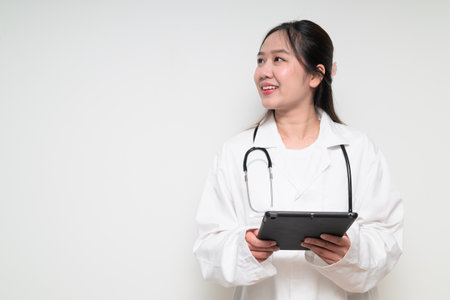 Studio portrait of Southeast Asian Thai healthcare worker woman doctor in lab coat against white background posing confidentlyの写真素材