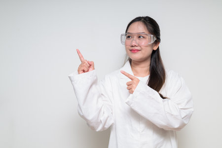 Portrait of Asian healthcare worker scientist woman in lab coat wearing safety goggle glasses against white background posing confidentlyの写真素材