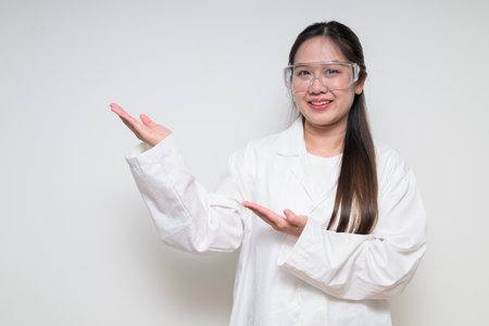 Portrait of Asian healthcare worker scientist woman in lab coat wearing safety goggle glasses against white background posing confidentlyの写真素材