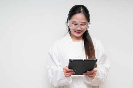 Portrait of Asian healthcare worker scientist woman in lab coat wearing safety goggle glasses against white background posing confidentlyの写真素材