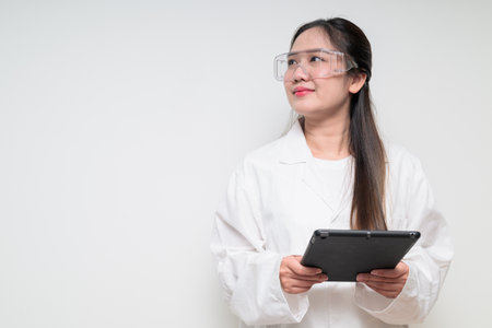Portrait of Asian healthcare worker scientist woman in lab coat wearing safety goggle glasses against white background posing confidentlyの写真素材
