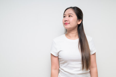 Studio portrait of young cute Asian woman thinking against plain background wearing casual white t-shirtの写真素材