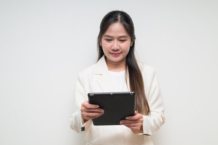 Studio portrait of young Asian woman wearing suit ready for business against white background using digital tablet computerの写真素材
