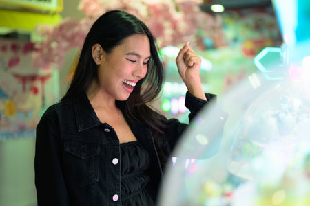 Happy young Asian woman playing arcade video games indoors and winning raising her arm
