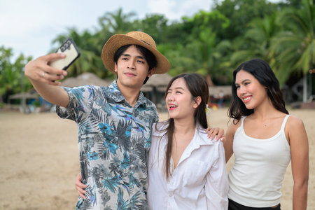 Three young Asian friends at beach taking selfie with mobile phone while having fun weekend trip holidayの写真素材
