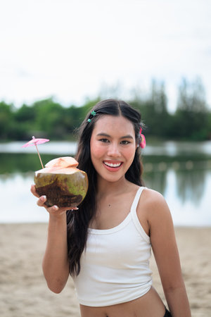 Portrait of beautiful young Asian woman at beach during summer holiday holding coconutの写真素材