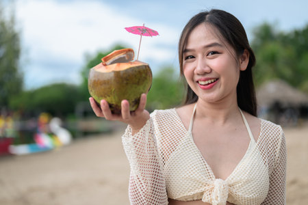 Portrait of beautiful young Asian woman at beach during summer holiday holding coconutの写真素材