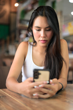 Beautiful young Asian woman sitting at restaurant using mobile phone texting