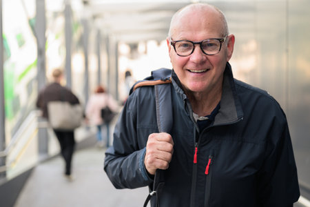 Portrait of happy senior man with backpack standing at the railway stationの写真素材