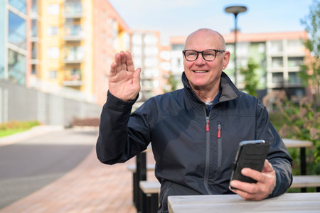Portrait of senior man with mobile phone waving hand while sitting
