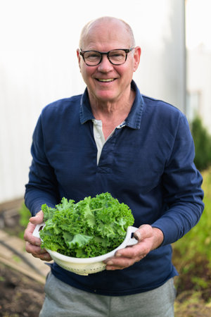 Portrait of a bald senior man holding a bowl of fresh kale in his garden during autumn