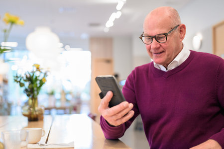 Portrait of a senior man with eyeglasses in a cafe using smartphone