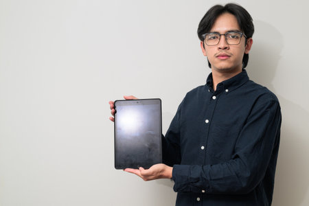 Portrait of handsome Young Asian Thai man in early 20s against showing copy space from tablet computerの写真素材