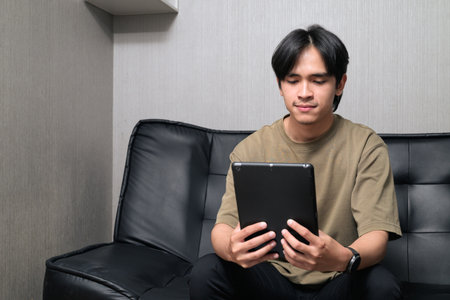 Portrait of handsome Young Asian Thai man using digital tablet computer at homeの写真素材