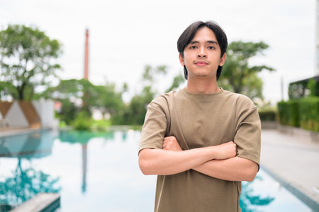 Portrait of handsome Young Asian Thai man in early 20s relaxing next to swimming pool on summerの写真素材