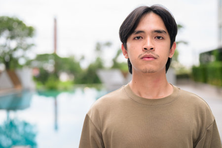 Portrait of handsome Young Asian Thai man in early 20s relaxing next to swimming pool on summerの写真素材